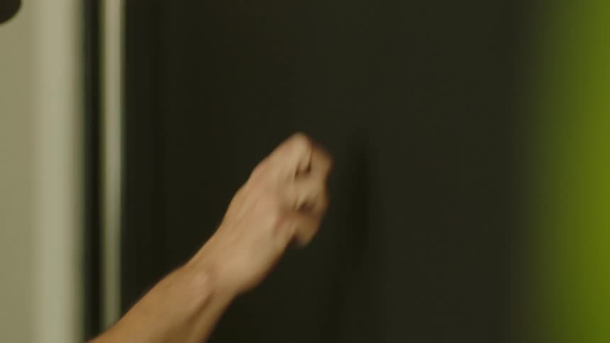 A hand with a clenched fist knocks on a darkcolored door