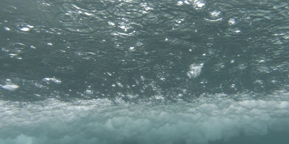 Rain falls on the water and a wave crashes