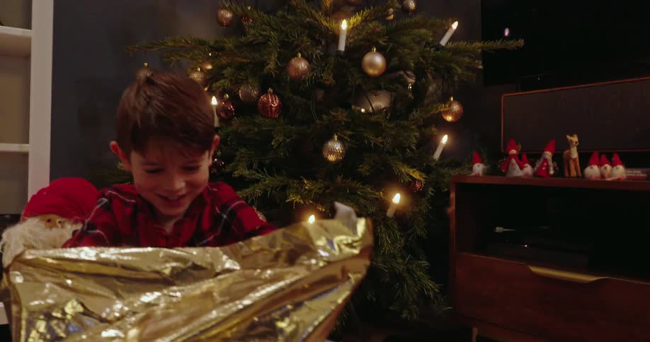 Excited young boy unwrapping a gift wrapped in gold wrapping paper on christmas morning