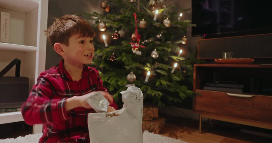 A child is talking and smiling while he opens christmas gifts