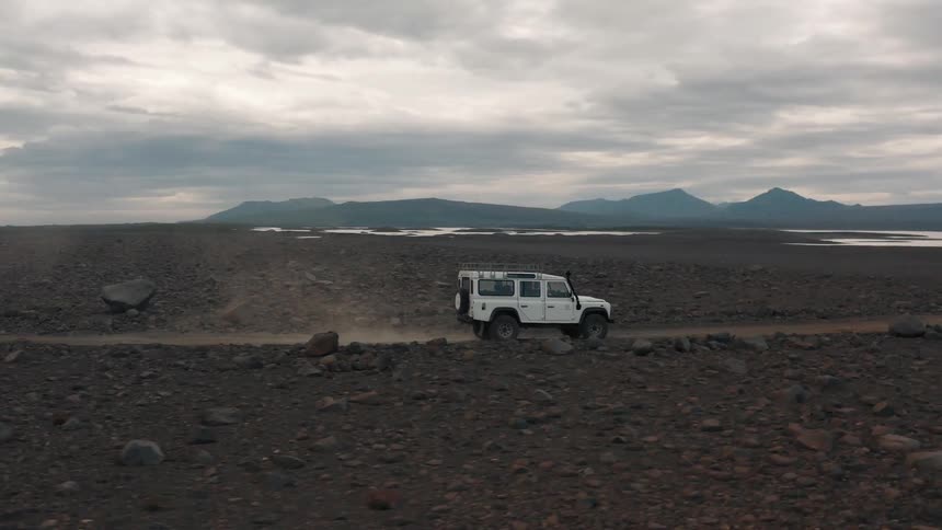 A white jeep traveling on a dirt road across a large dirt covered landscape