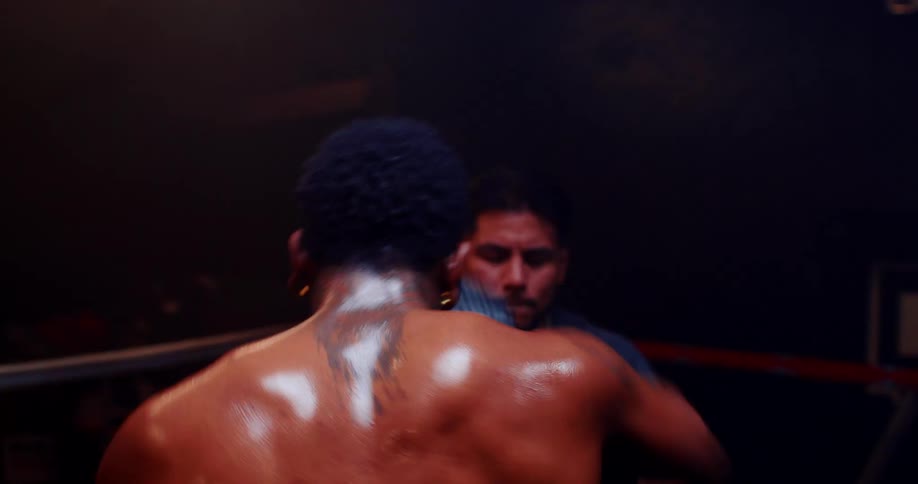 Male boxer sweats while standing in the boxing ring and working with his trainer