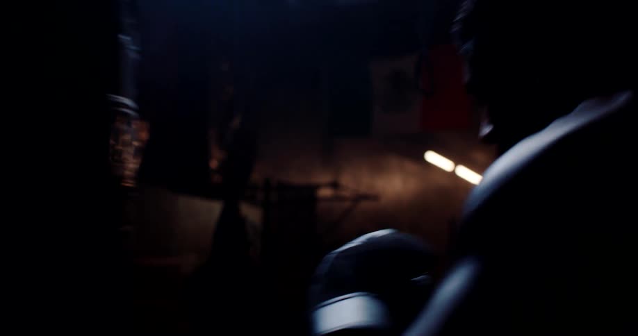 A closeup of a boxer in a dimly lit gym wearing gloves practicing punches on a heavy bag