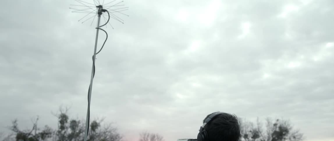 A man is sitting in front of a metal pole on a cloudy day