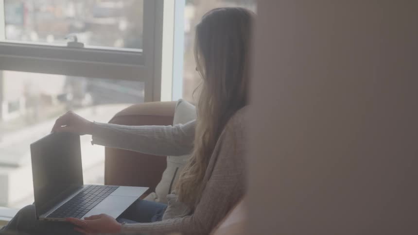 A woman sitting on the couch opens her laptop