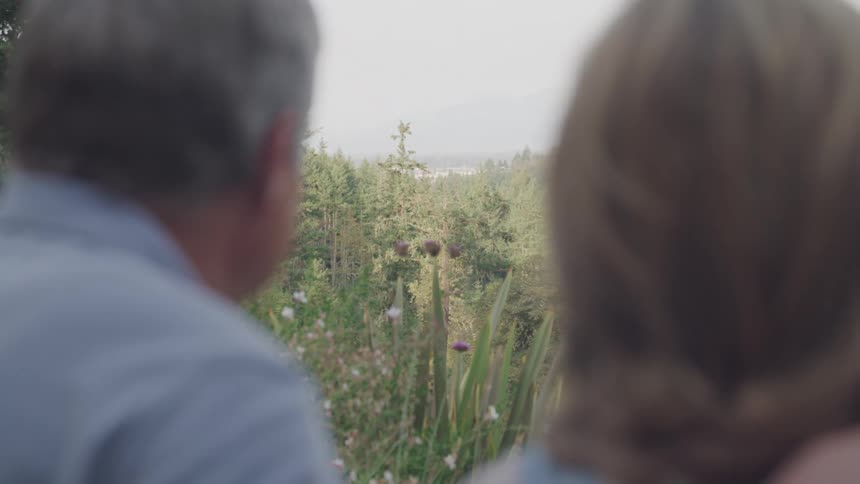 A couple look out over a garden and forest