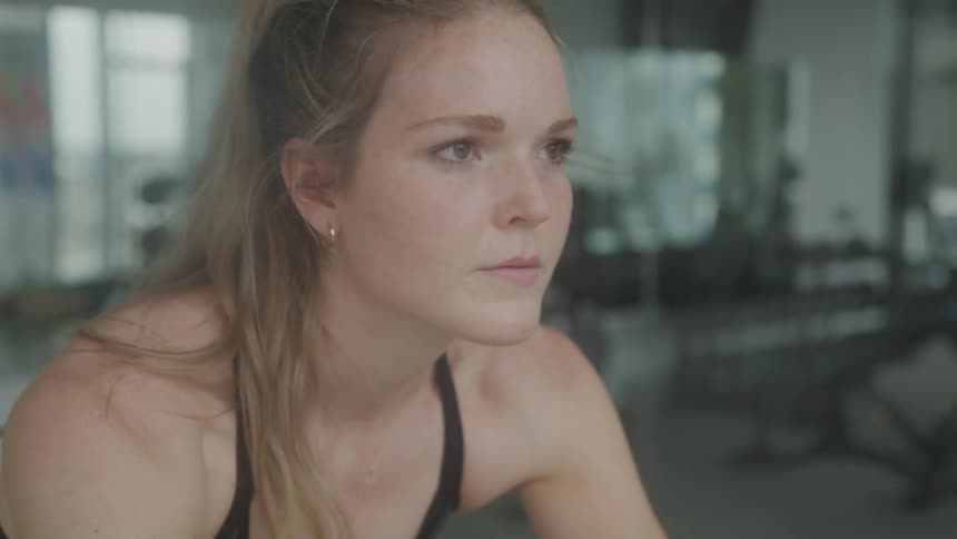 Woman pedals on a stationary bicycle while in a gym during the day