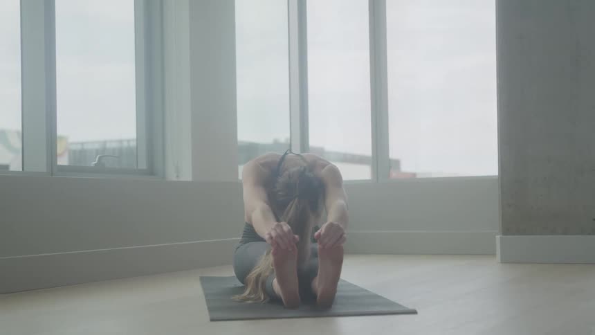 Near windows a woman is stretching in an empty gym