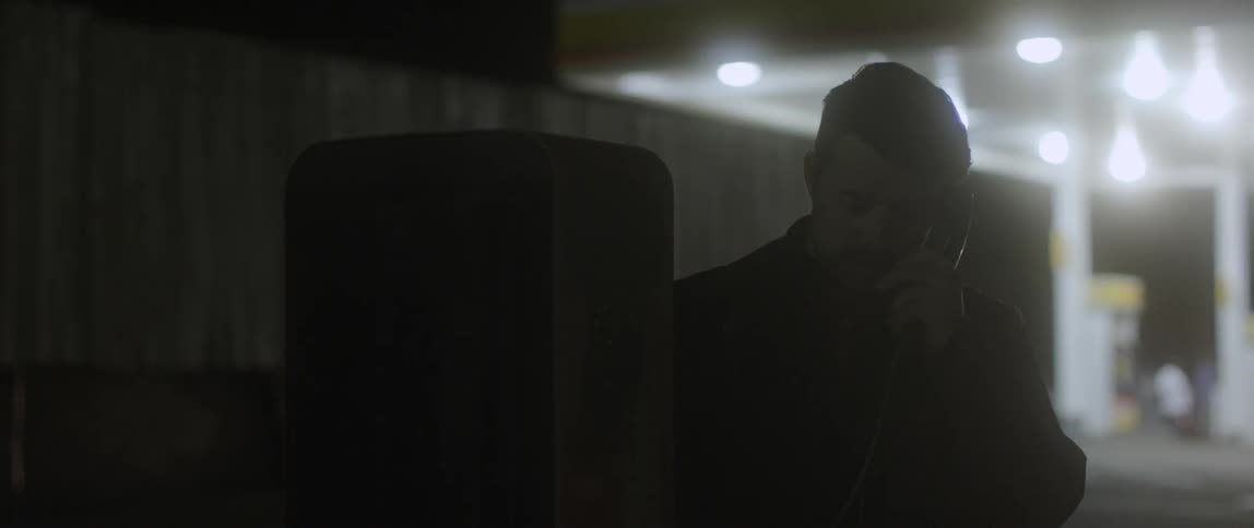 A man talks on a payphone at night