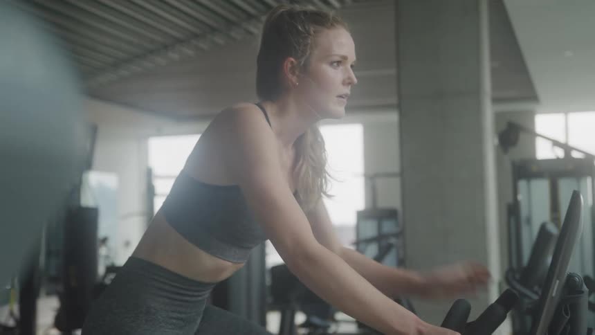 A female is exercising on a stationary bike in a gym