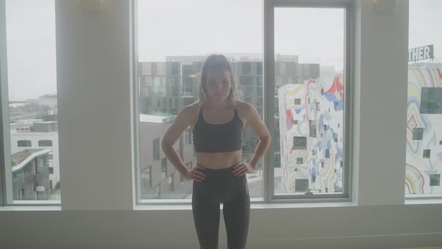 A woman is standing with her hands on her hips by the window