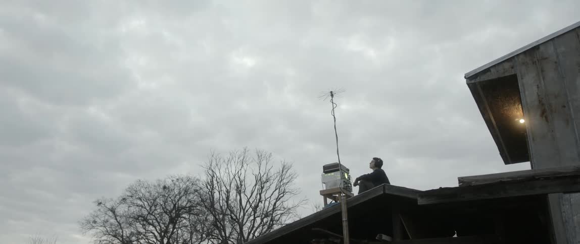A man sitting on a roof looking up at the cloudy skies