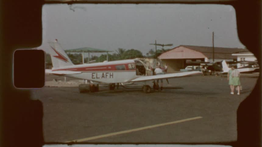 People walk around a small plane parked at an airfield on a summer day