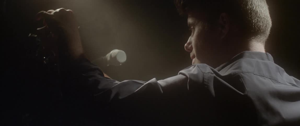 A man is setting up a microphone on a dark stage