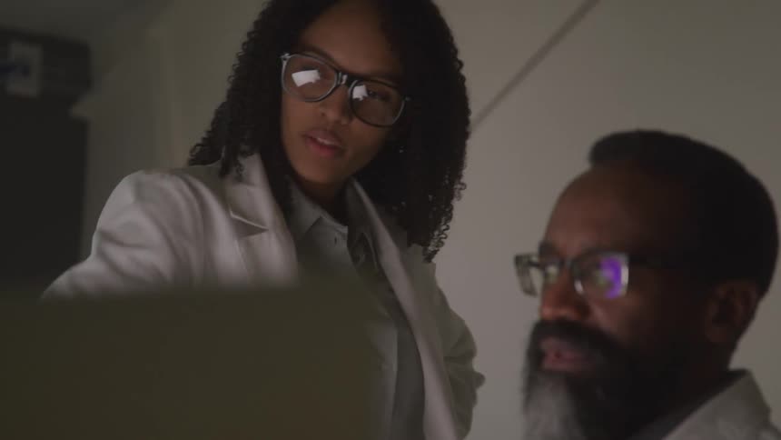 Two individuals in lab coats and glasses appear to be examining something out of frame