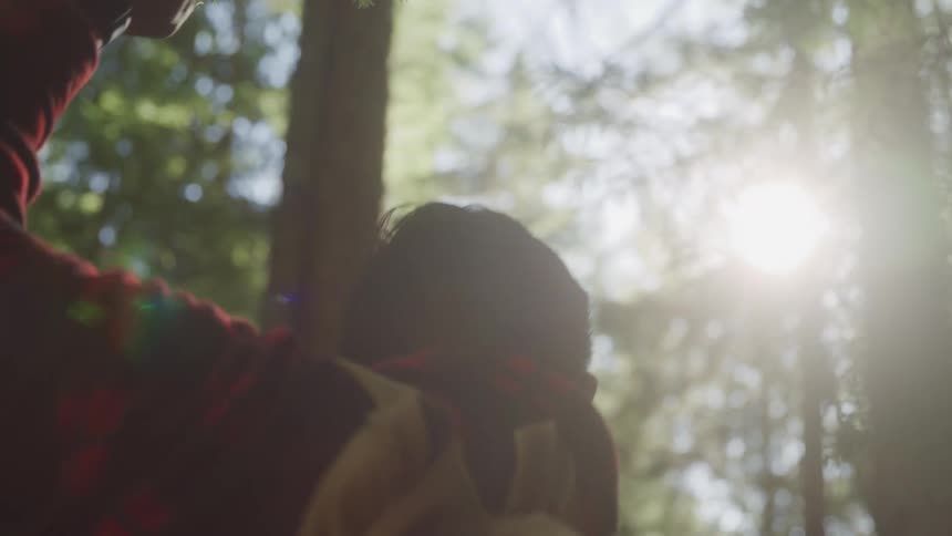 Man wearing a red plaid jacket and a brown backpack hikes in the forest