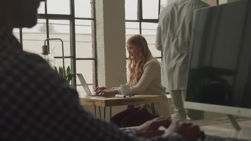 A woman typing on a laptop while a coworker walks by
