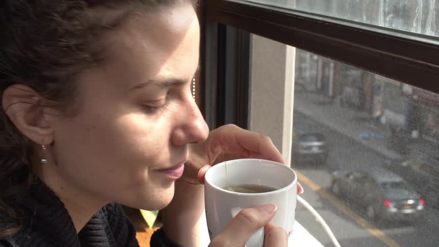A woman is enjoying a warm beverage as she looks out the window