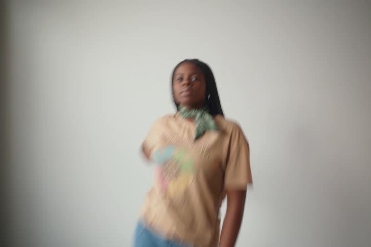 A young teenager stands confidently in front of a plain white backdrop wearing a tshirt jeans and a patterned scarf around their neck