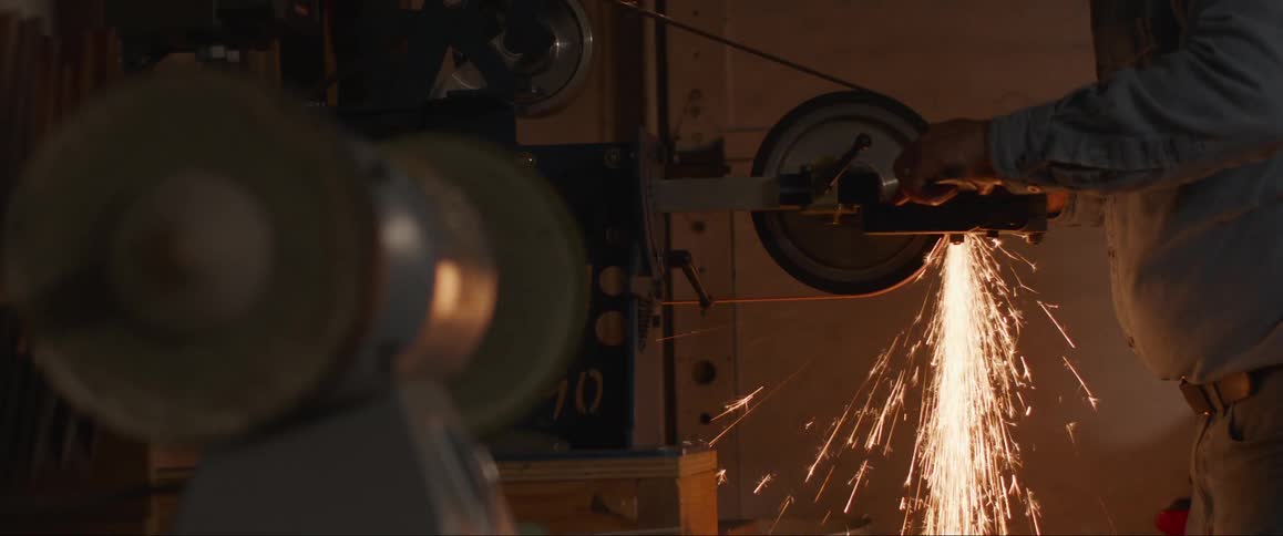 A worker operates a grinding machine creating a vivid spray of sparks as it cuts into a metal object