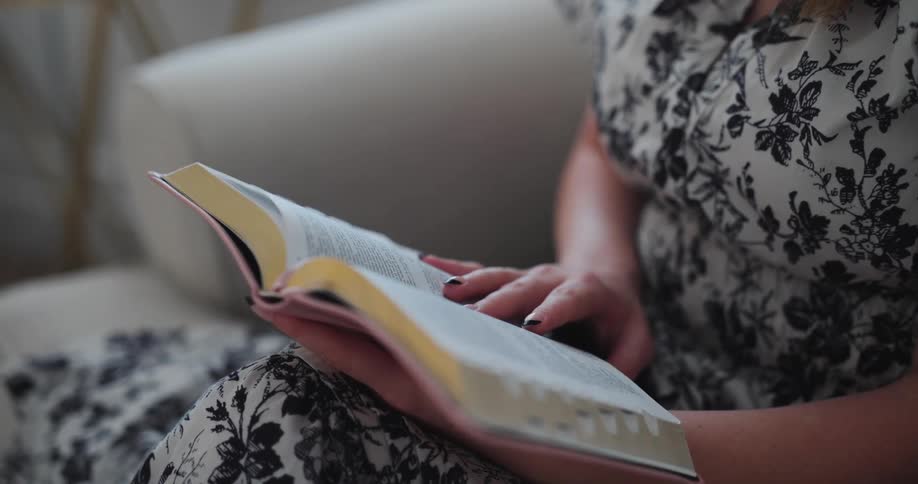 Woman wearing black and white floral dress sitting on couch reading a book