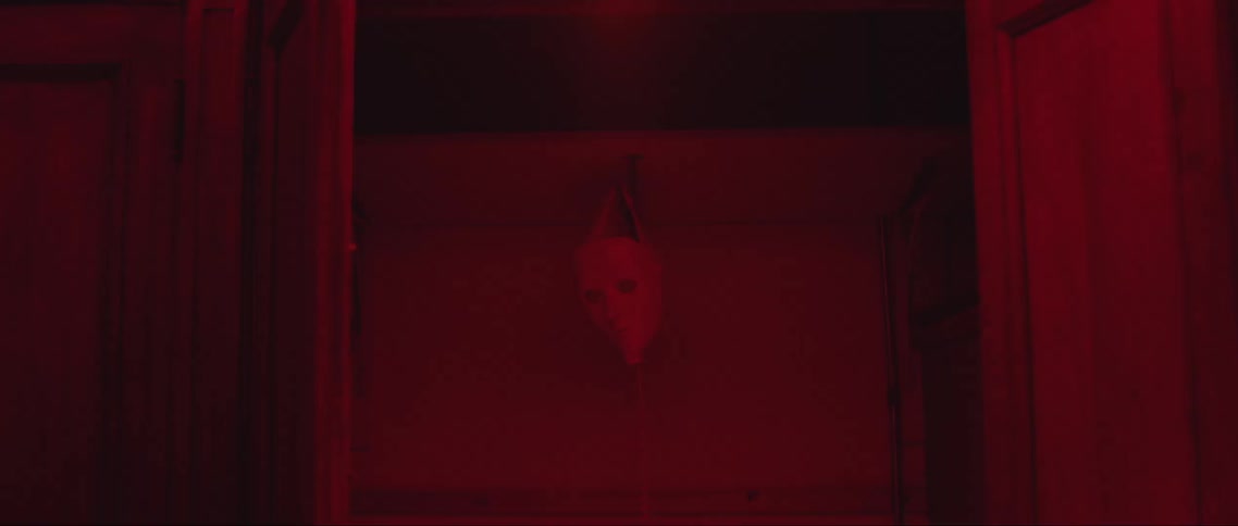 Mask hangs from a hook in a room lit by red lighting