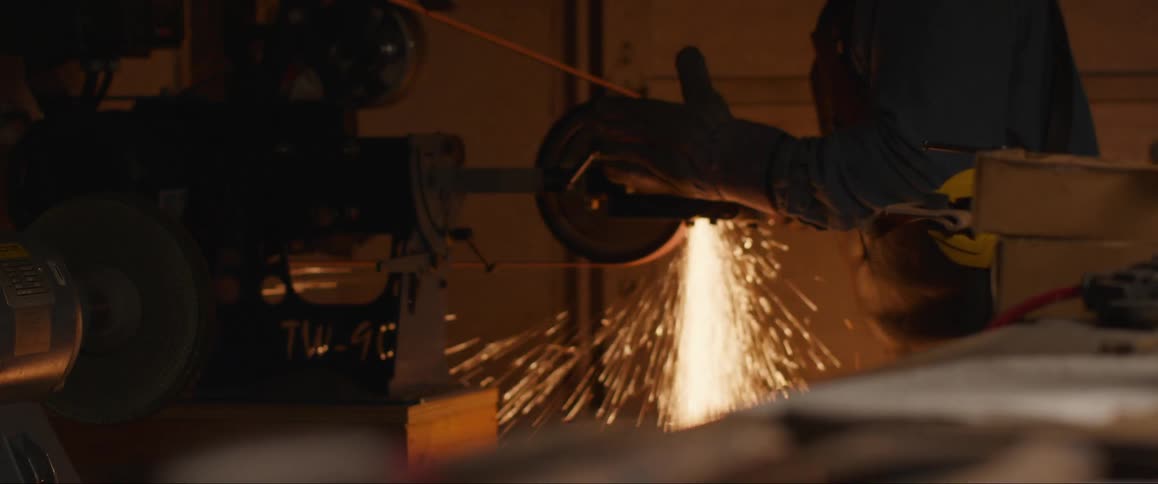 A worker operates a grinding machine sending bright sparks flying in all directions