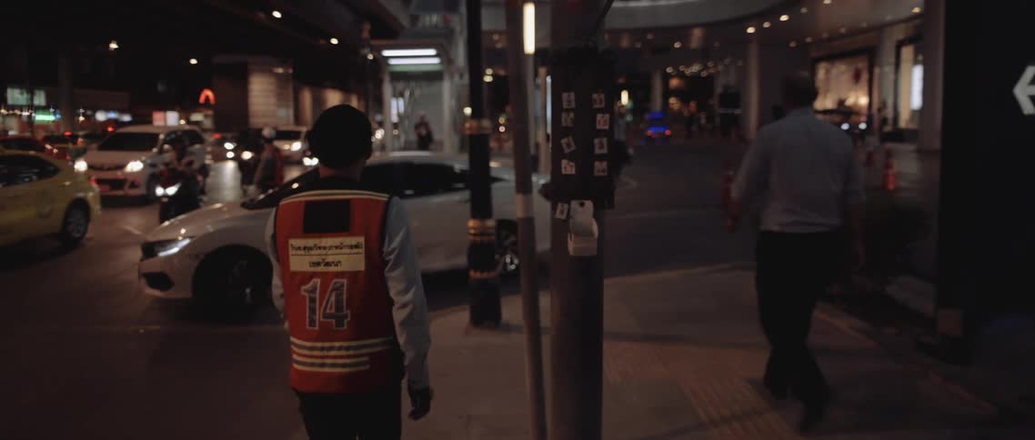 At night a person wearing a numbered safety vest stands near traffic on a bustling city street