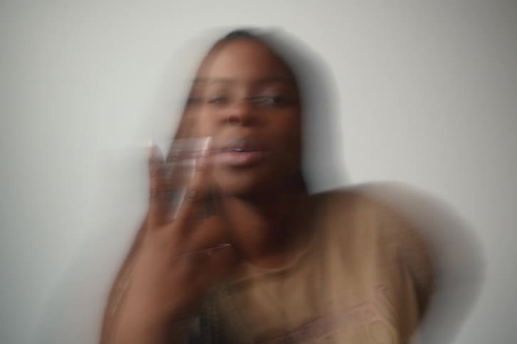 An extremely shaky closeup of a woman smiling with her fingers making a victory or peace sign against a white background
