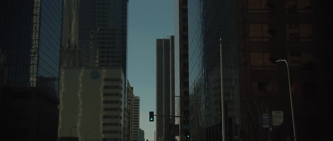 Traffic lights glow between towering skyscrapers in the city under a clear morning sky