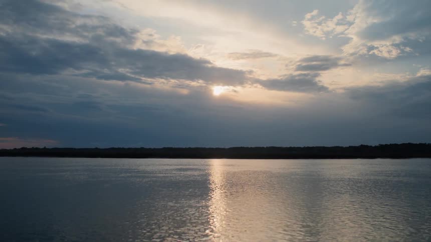 Sun reflecting across the lake behind the clouds as it sets at dusk