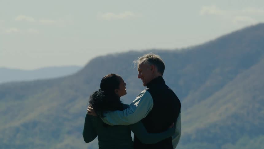 A man and woman hug while looking at a mountain range