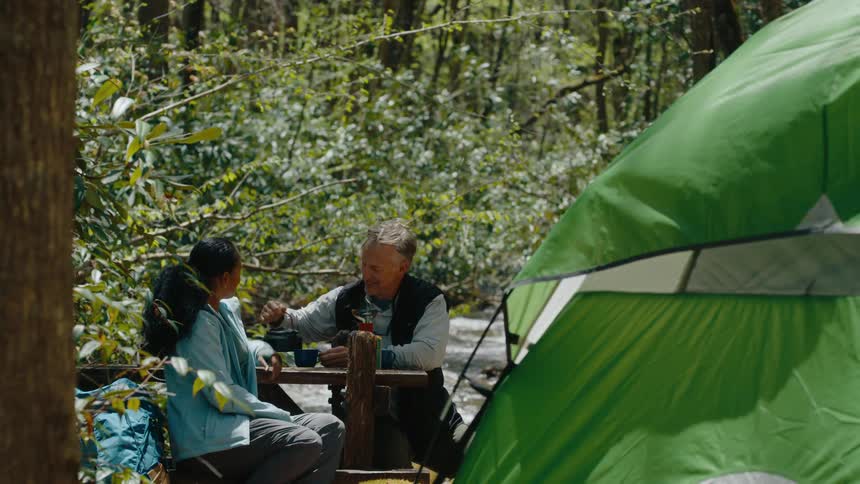 A man and woman drink together while camping