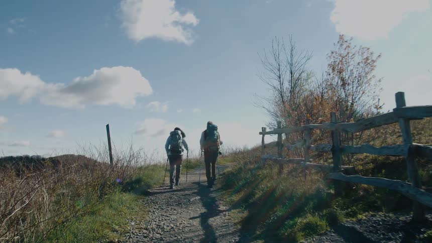 Hikers hiking on a dirt road in the hills alongside a rustic wood fence