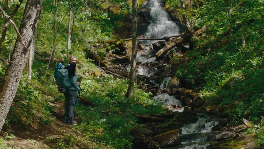 A man and woman are hiking past the small stream