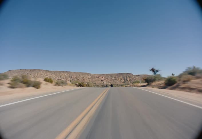 Two motorcycles drive on a desert road