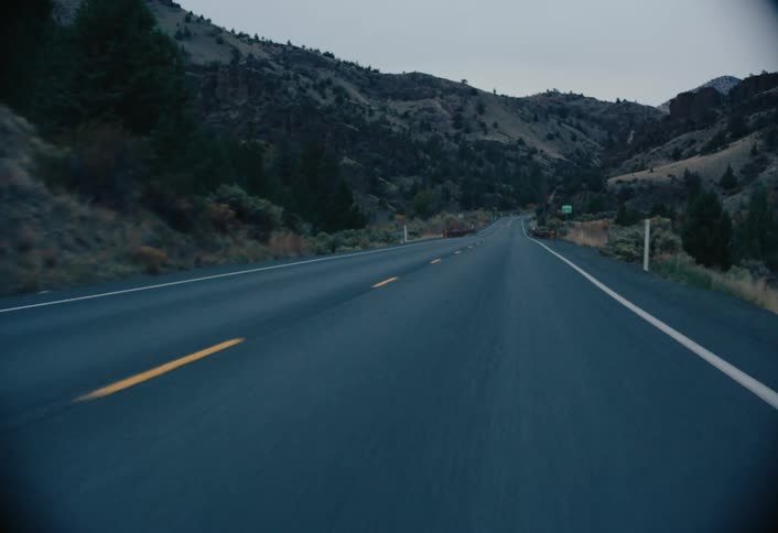 An empty asphalt road stretching into the distance framed by hills on either side