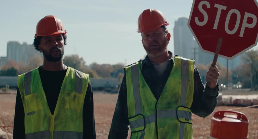 Two male workers one of them holding a stop sign exchange glances while standing near a field in the autumn