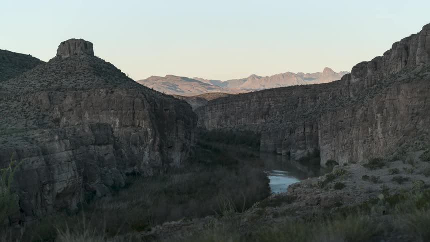 A sunlit canyon with steep rocky walls framing a river flowing through its depths under a clear sky