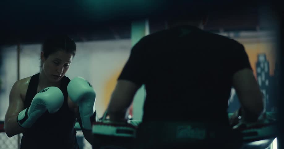 Female kick boxer trains in a ring at the gym with her trainer