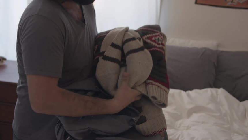 Man puts laptop and clothes into a backpack
