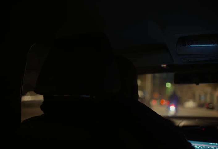 A person is riding in the back of a car the driver is talking the camera pans out on the drive to a train