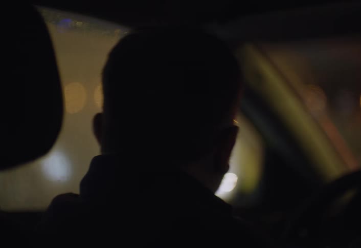 A man is driving a car during the night time while its raining