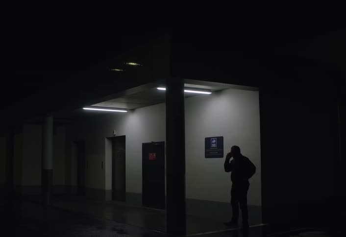 Man talking on a cell phone while pacing in a dimly lit hallway