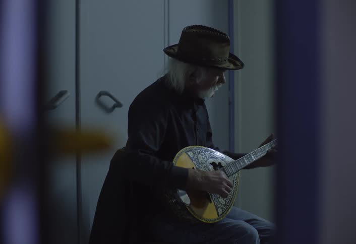 Elderly man sits alone indoors and plays a lute