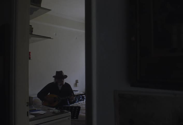 A man is sitting on his bed playing the guitar