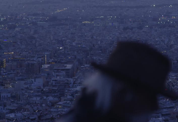 The camera pans over a vast cityscape while a man in the foreground smokes