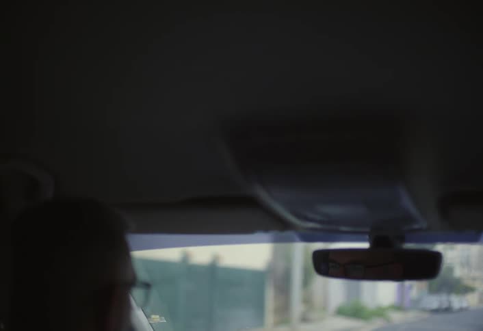 The interior view from the front of a vehicle focusing on the rearview mirror and the slightly blurred scene outside the windshield