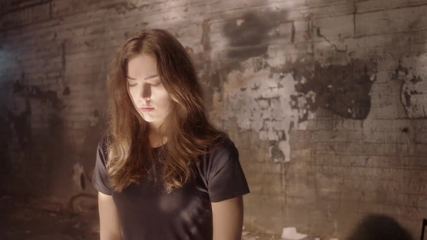 A woman in a building as the sun shines on her and she looks sad