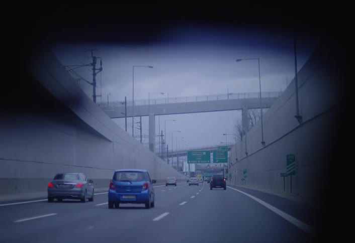 Vehicles drive through a dimly lit tunnel towards an exit revealing an overpass and highway signs